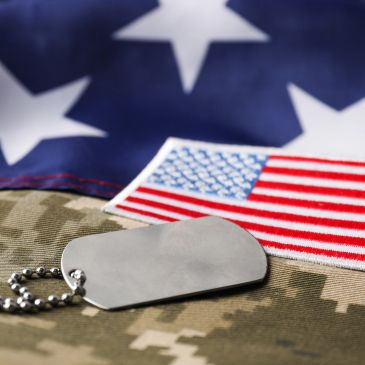 Military dog tag on camouflage uniform with American flag patch.