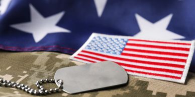 Military dog tags and American flags on camouflage fabric.