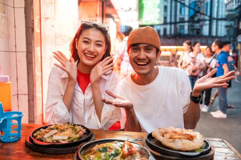 Asian couple man and woman enjoy eating street food noodle at night market. Traveler Asian couple blogger Happy tourists with Traditional food local road at thailand bangkok city.