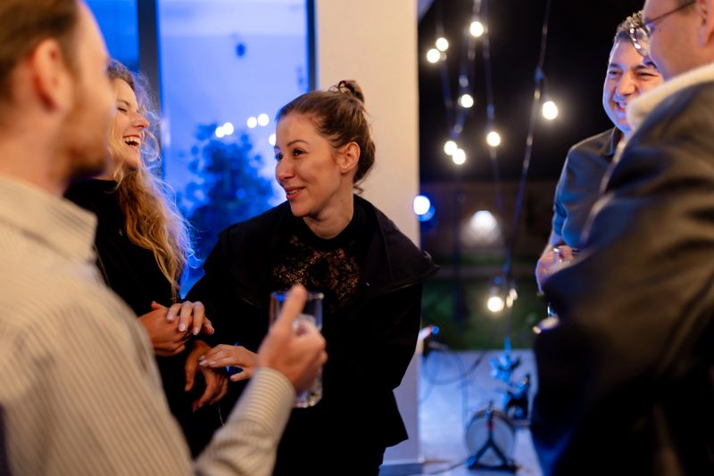 A cheerful group of friends enjoy lighthearted conversation at an outdoor evening party, illuminated by festive lighting, showcasing warmth, companionship, and a convivial atmosphere.