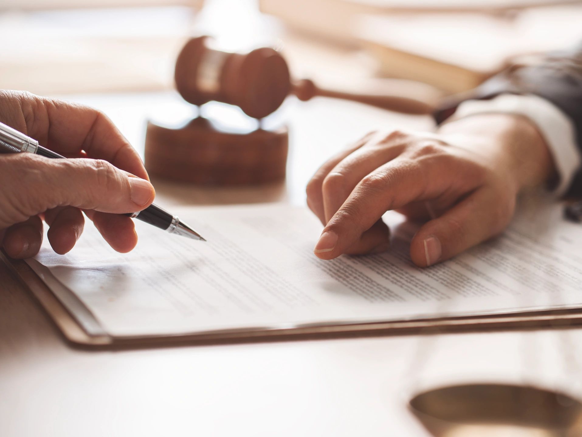 Person signing legal document with judge's gavel in background.