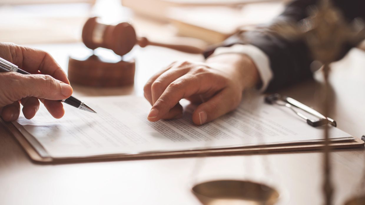 Two people reviewing and signing a legal document with a gavel in the background.