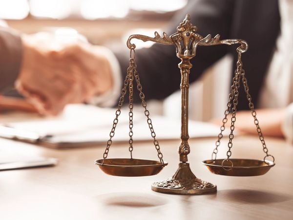 A golden justice scale with handshake in background.