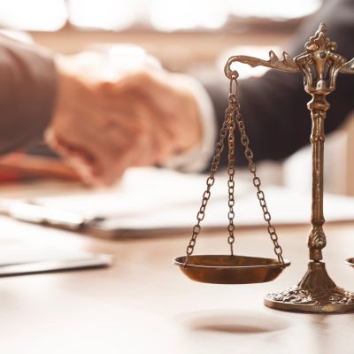 Handshake behind a justice scale symbol on a desk.