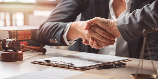 Two professionals shaking hands over legal documents at a desk.