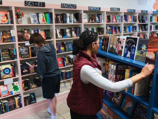 Two people browsing books in a cozy bookstore with genre signs.