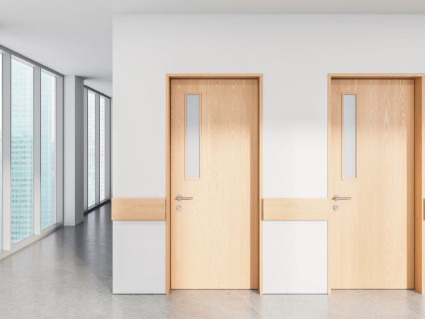 Two wooden doors in a modern hallway with large windows.