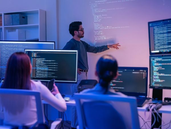 Man presenting coding concepts to colleagues in a modern office setting.