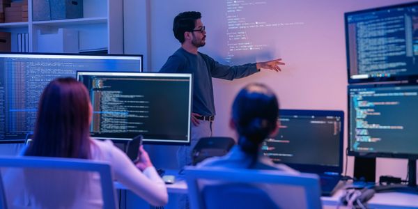 Persona dando una presentación de programación en sala con varios monitores.