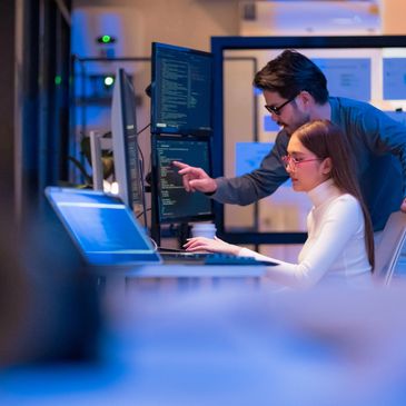 Two professionals collaborating on coding at a computer workstation.