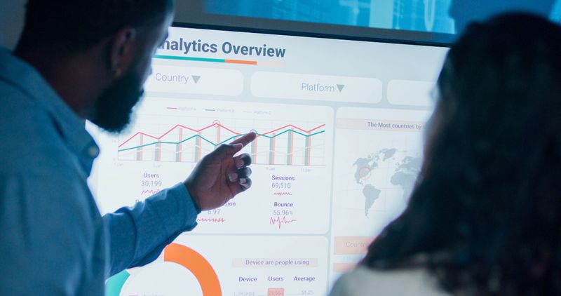 Closeup group of business professionals meeting working late discussing strategy and analyzing data on large screen, collaborating on business growth standing at office night. Finance meeting concept.