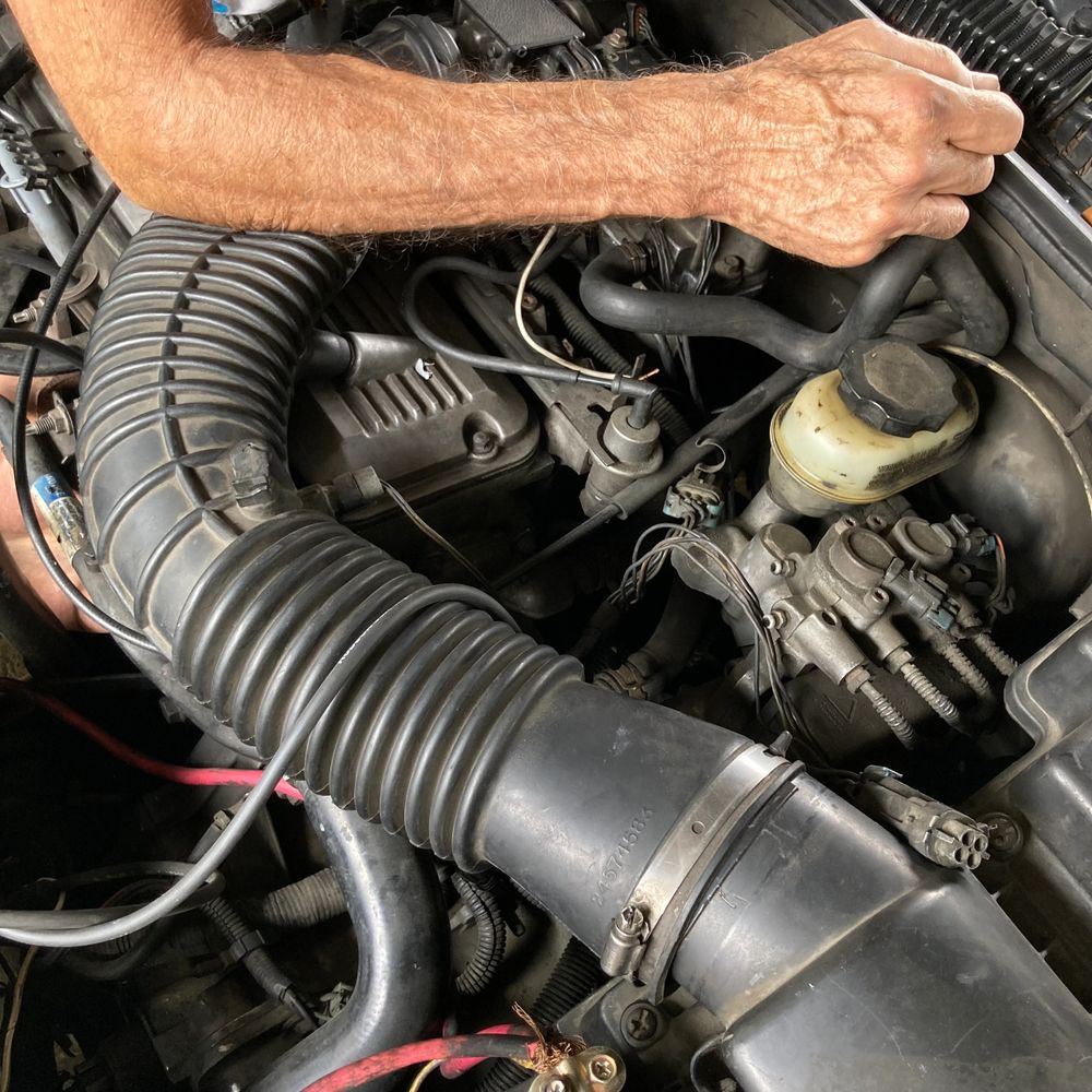 A person working on a car engine with visible hoses and wires.