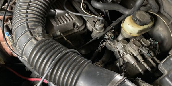 A person working on a car engine with visible hoses and wires.