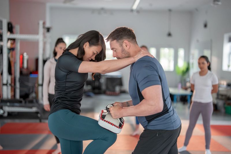 Women participate in a self-defense class practicing martial arts techniques under expert guidance. The session emphasizes empowerment, practical skills, and safety in a supportive group environment.