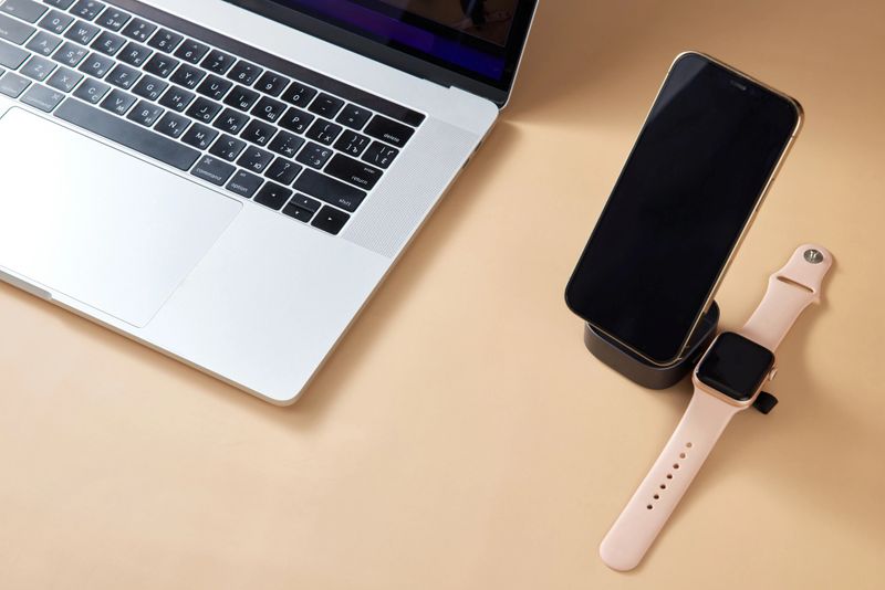 open laptop with smart watch and smartphone charging on wireless charger on beige table, Modern workplace device