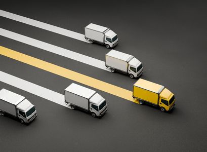 Yellow truck stands out among white trucks on striped road.