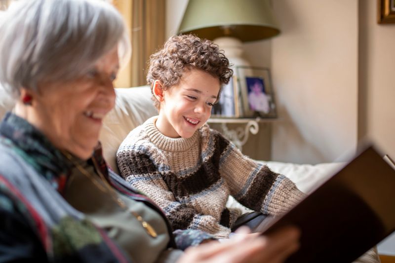 Grandmother and grandchild sharing a tender moment reading a book together on a sofa, enjoying quality time and creating lasting memories