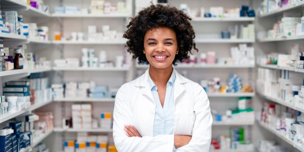 Smiling pharmacist standing confidently in a well-stocked pharmacy.