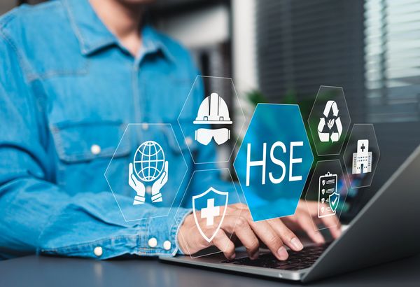 Person typing on laptop with HSE icons representing health, safety, and environment.