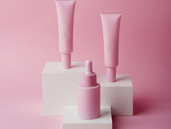 Minimalist pink cosmetic tubes and dropper bottle on white blocks.