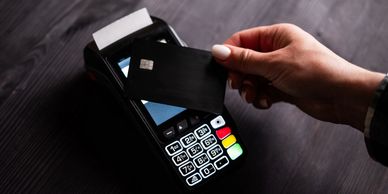 Hand holding card near payment terminal for contactless payment.