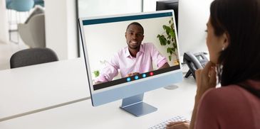 Woman video chatting with a man on a desktop computer in an office.