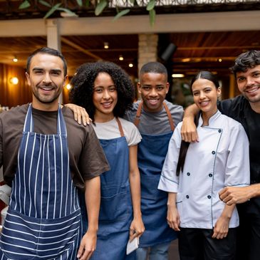A group of five diverse chefs smiling together in aprons and chef coat.