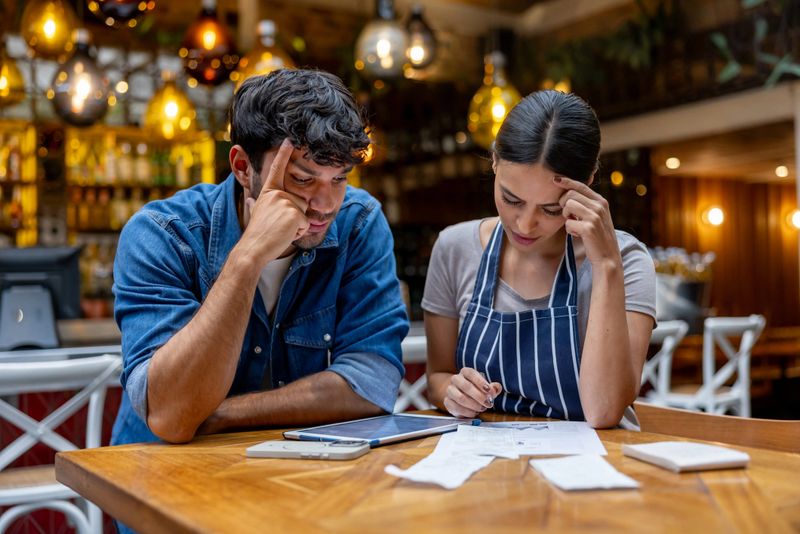 Business owner and waitress doing the accountancy at a restaurant and looking worried - small business concepts