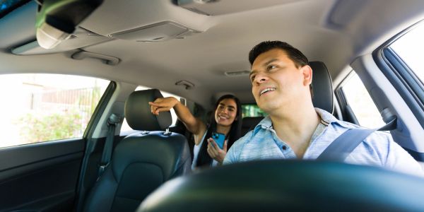 Man driving with a smiling woman pointing in the back seat.