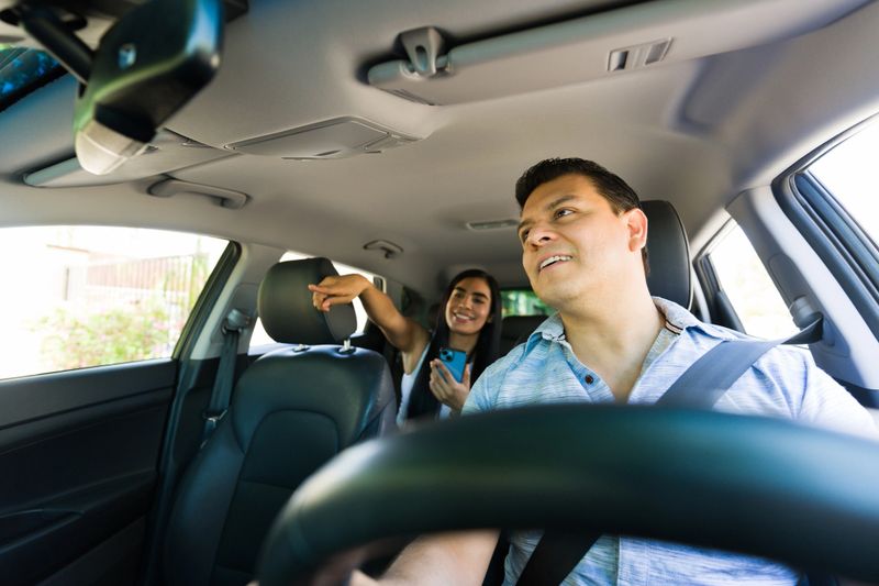 Hispanic driver following a gps route while passenger shows directions on a smartphone app in a rideshare service