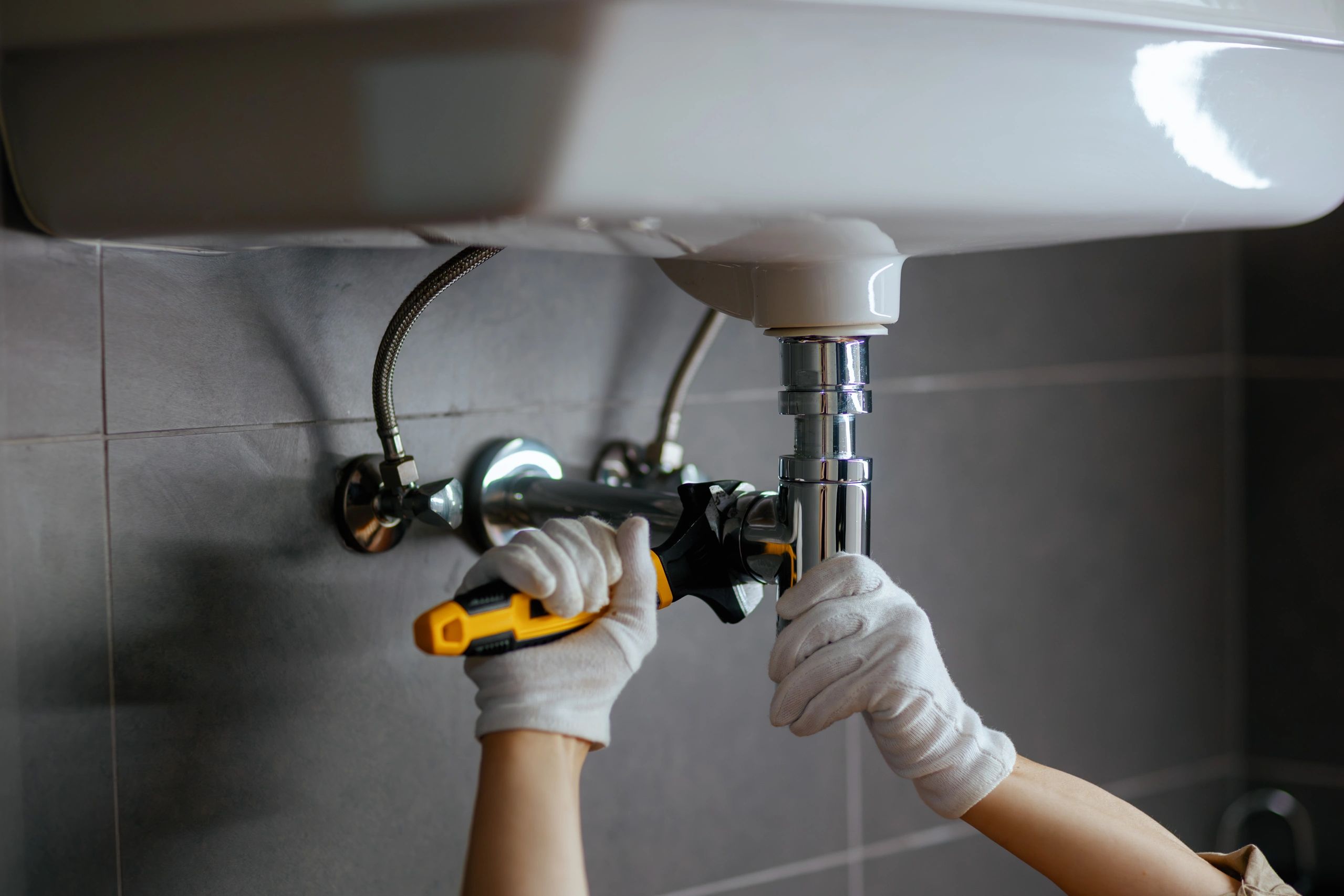 Person fixing a sink pipe with a wrench.