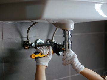Plumber fixing a pipe under a sink with a wrench.