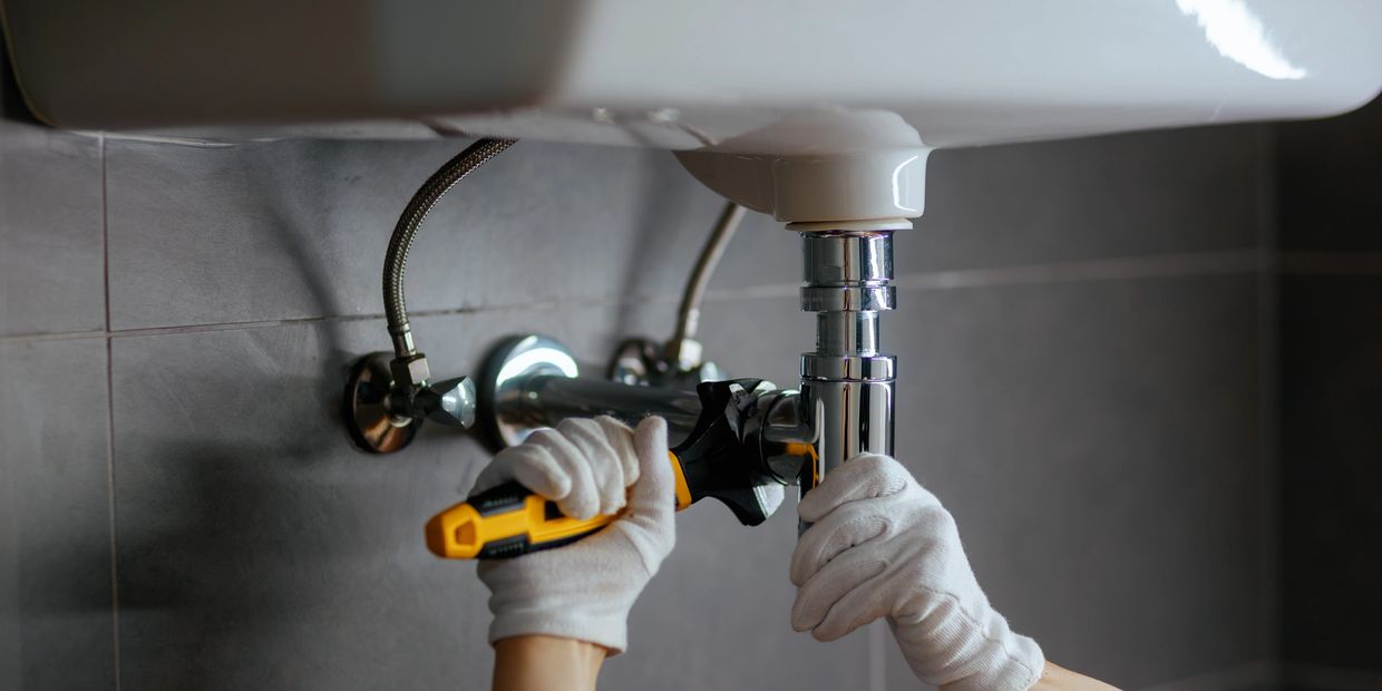 Person fixing a bathroom sink pipe with a wrench.