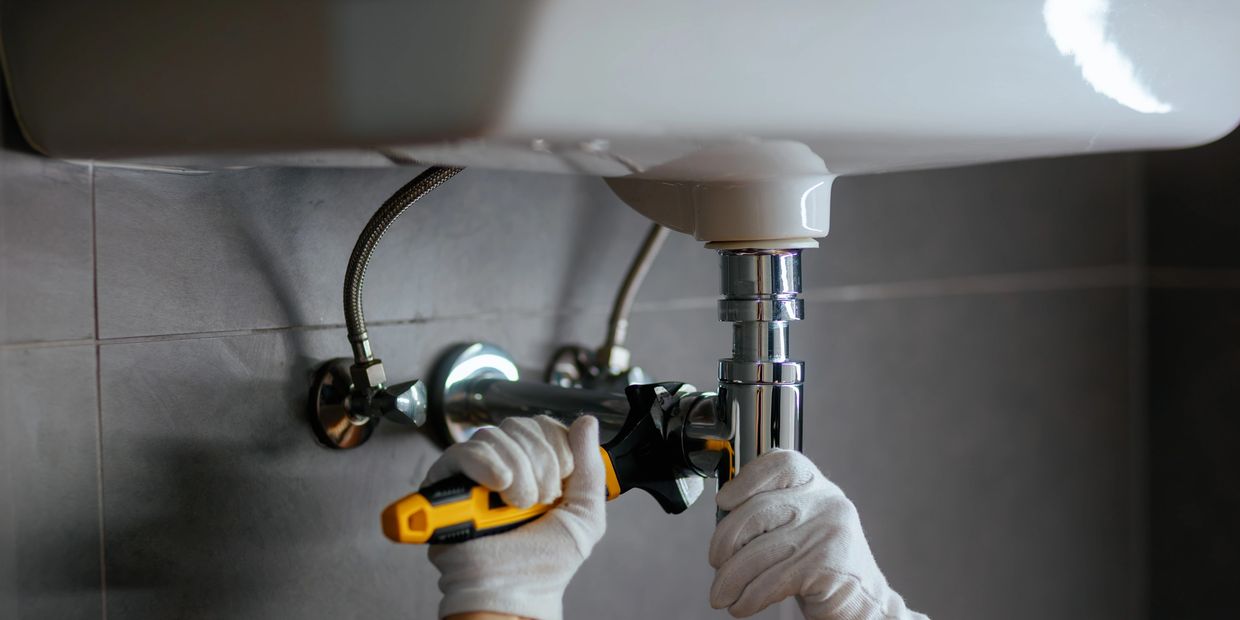 Person fixing a bathroom sink pipe with a wrench.