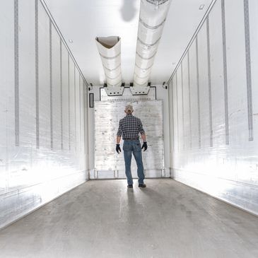 Man stands inside an empty refrigerated truck trailer.