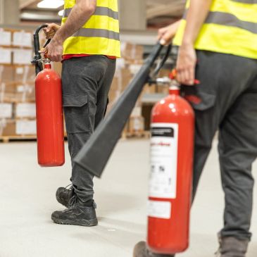 Workers carrying fire extinguishers in a warehouse.