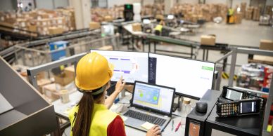 Worker overseeing production with multiple screens in a warehouse.