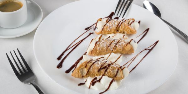 Three cannoli on a white plate with coffee.