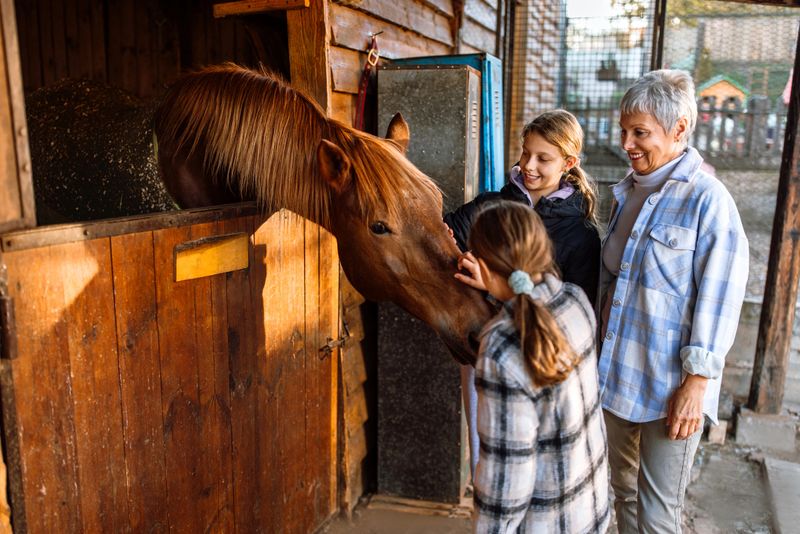Grandmother and granddaughters petting horse at farm