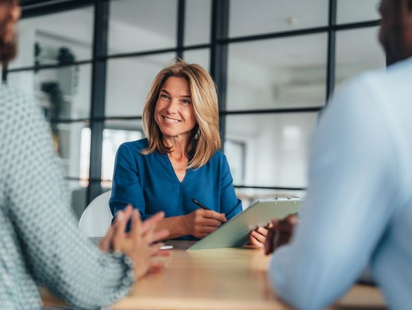 Smiling woman holding a clipboard during a meeting with two colleagues.