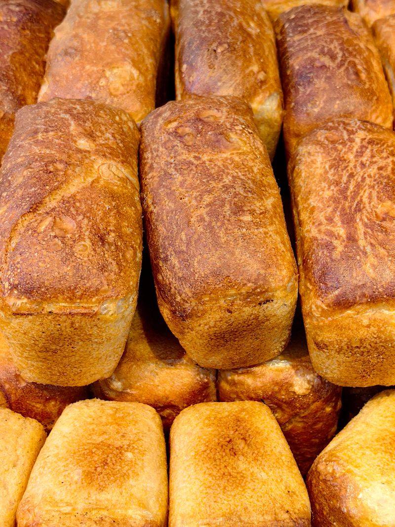 variety golden-brown artisanal bread loaves sit neatly stacked in local bakery. warm, inviting scent fills air as afternoon light highlights their texture. close up.