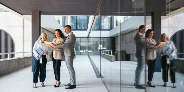 Three professionals discussing documents in a modern office corridor.