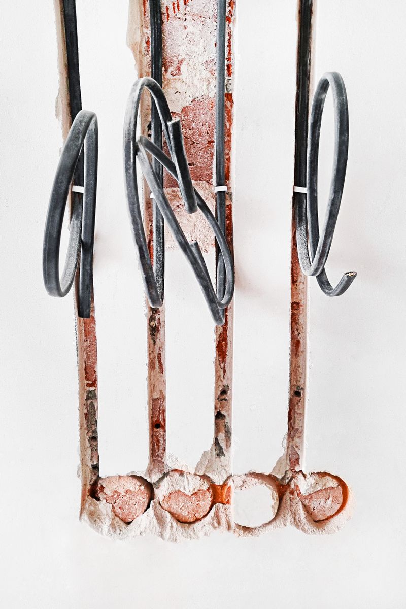 Exposed electrical wiring during a home construction or house renovation improvement project with looped black cables in conduit trench lines in white unfinished wall with bricks, mortar and plaster