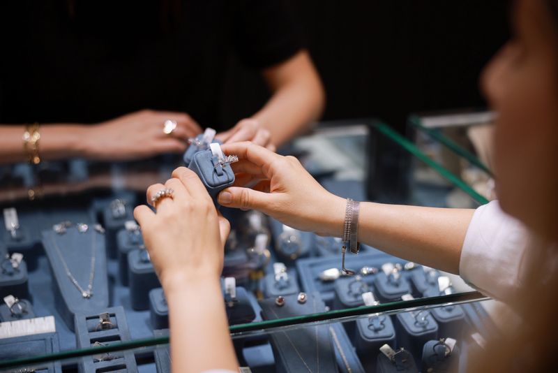 Luxury jewelry store concept. Hand of woman customer trying diamond gold ring for wedding in jewellery shop. Five-stone diamond ring