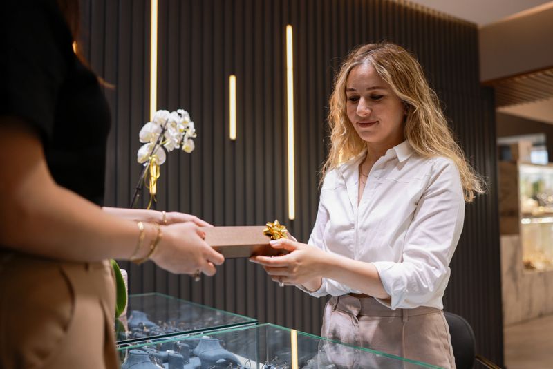Close up of saleswoman handing shopping bag to customer in jewelry store. Woman shopping jewelry in the store, talking with saleswoman