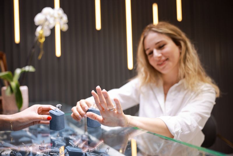 Luxury jewelry store concept. Hand of woman customer trying diamond gold ring for wedding in jewellery shop. Five-stone diamond ring