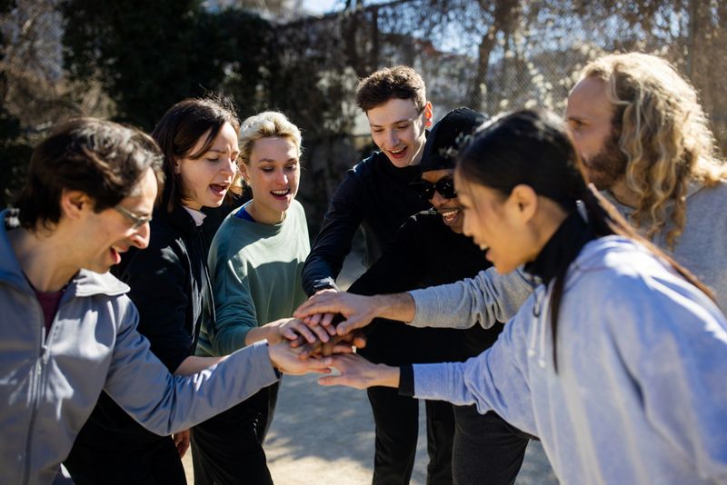 Group putting their hands together while smiling on urban sports court. Team exhibiting unity by connecting their arms and having a good time outdoors.