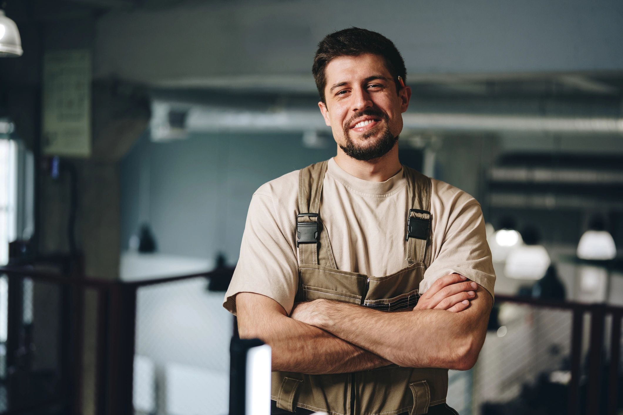 Smiling man in work overalls with crossed arms in an industrial setting.