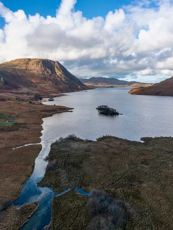 Serene lake surrounded by hills under a partly cloudy sky.
