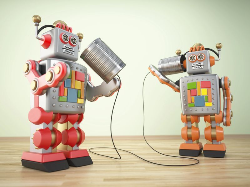 Two colorful toy robots are using tin cans connected by string to communicate in a playful environment. Brightly designed, they demonstrate creativity and fun.